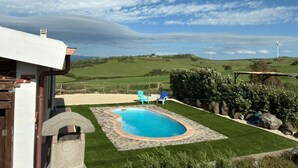 A pool with a stone border, a wooden deck, and a view of wind turbines in the distance. - Sos Giajos Rural house (Nulvi)