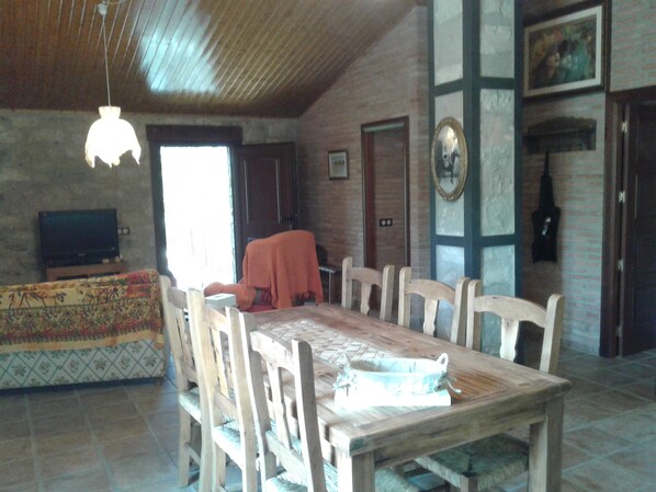 Un comedor con una mesa y sillas de madera, un televisor sobre un mueble bajo y un sofá estampado.