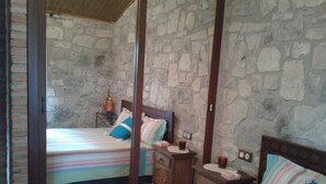 Un dormitorio con dos camas, una pared de piedra, muebles de madera y una mesita con una lámpara.