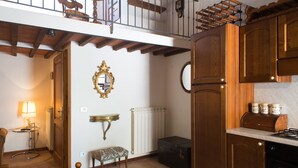 A kitchen with wooden cabinets, a dining table, a bench, a radiator, and a staircase leading to an upper level. - San Gimignano Apartment in the Heart of the City for 3 People: Fast Wi-Fi, Concierge Service (San Gimignano)