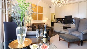 Un salon moderne avec une table basse en verre, un vase orné de branches, une bouteille de champagne et un canapé.