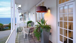 Un espace extérieur abrité, équipé d’une table et de chaises, d’une plante en pot et d’une porte portant l’inscription « A ».