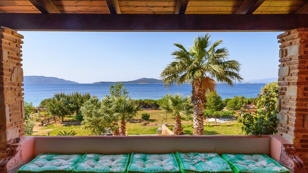 Un balcón con vista al mar, palmeras y un paisaje con césped.