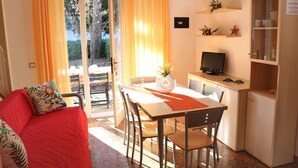 Ein gemütliches Zimmer mit einem roten Sofa, einem Esstisch mit Stühlen, einem kleinen Fernseher und einem Schrank.