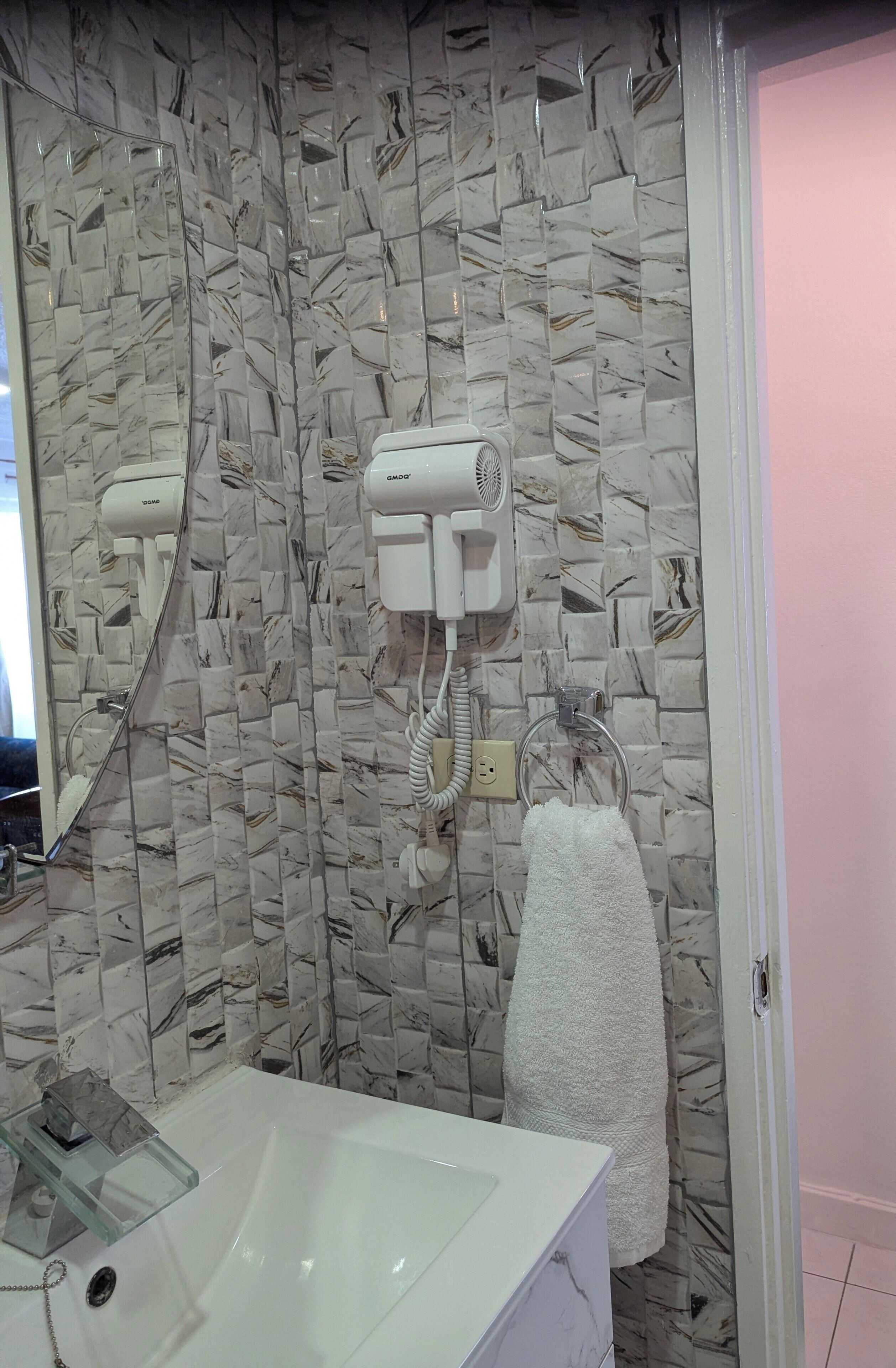 Une salle de bain avec un mur décoré d’un motif imitant le marbre, un lavabo en verre, un porte-serviettes et un sèche-cheveux.