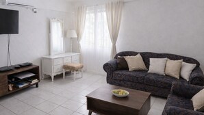 A living room with a sofa, a coffee table, a TV, a dresser, and a window with curtains. - Cosy & Stylish Studio at Turtle Beach Towers - Pool, Beach & Town Nearby  (Ocho Rios)