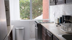 A modern kitchen with dark wooden cabinets, a stainless steel refrigerator, a built-in oven, and a window with a view of greenery outside. - Cosy & Stylish Studio at Turtle Beach Towers - Pool, Beach & Town Nearby  (Ocho Rios)