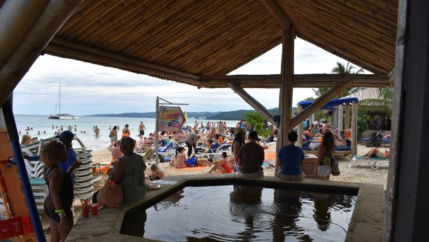 Un espace piscine situé au bord de la plage, avec une terrasse en bois et des chaises longues.