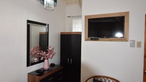 Une pièce avec un grand miroir, une armoire en bois, une commode noire, une petite table avec un vase, une chaise en bois et une fenêtre avec un cadre en bois.