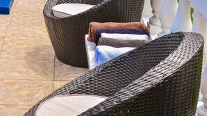 Deux fauteuils de jardin en osier, dotés de coussins, sont placés sur une terrasse carrelée, juste à côté d’une piscine.