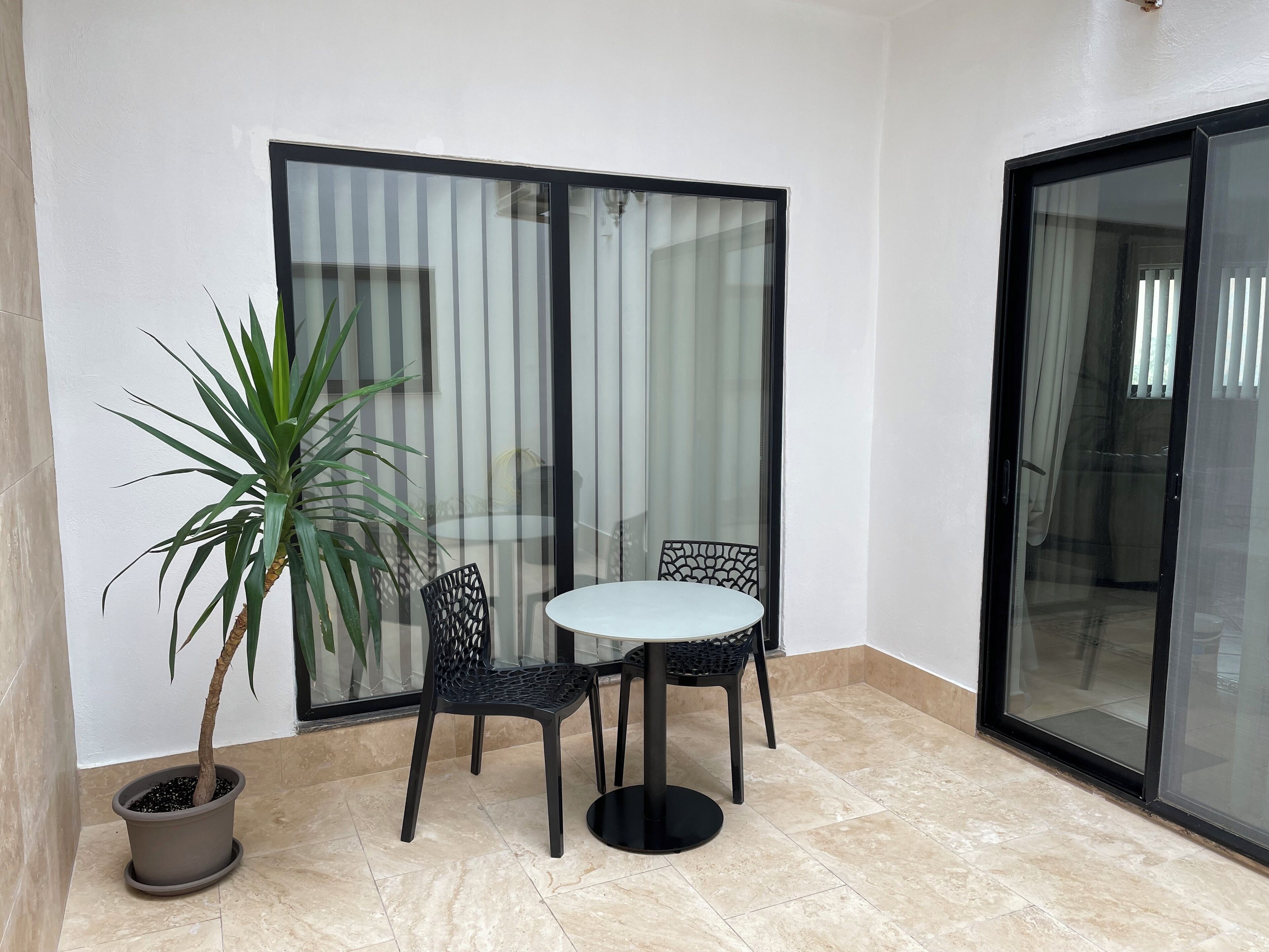 A small patio area with a round table and two chairs, a potted plant, and a sliding glass door.