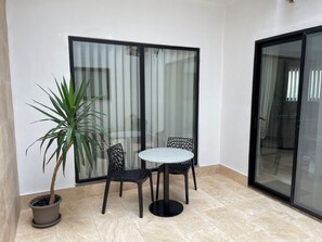 Un petit espace patio avec une table ronde et deux chaises, un pot de fleurs et une porte-fenêtre coulissante.