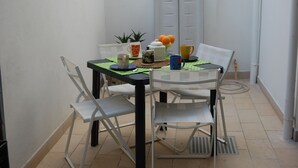 Een gezellig eetgedeelte met een tafel voor twee, met een witte tafelkleed, twee witte stoelen, een zwart tafelonderdeel en een kleine potplant.