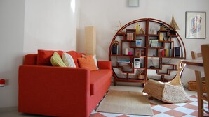 Een woonkamer met een rode bank, een houten boekenkast en een gevlochten mand.