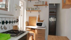 Een kleine keuken met een gasfornuis, magnetron en houten planken erboven.