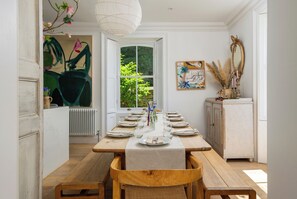 Een eetruimte met een houten tafel gedekt voor zes personen, een witte radiator en uitzicht op groen.