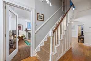 Una escalera con balaustres blancos y un suelo de moqueta color beige. Un cuadro enmarcado cuelga de la pared sobre la escalera.