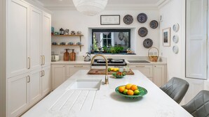 Een moderne keuken met witte kasten, een marmeren aanrecht, een groot schiereiland met een spoelbak, en diverse decoratieve borden aan de muur.