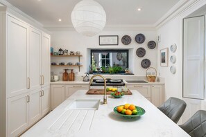 A modern kitchen with white cabinetry, a marble countertop, a large island with a sink, and a variety of decorative plates on the wall.
