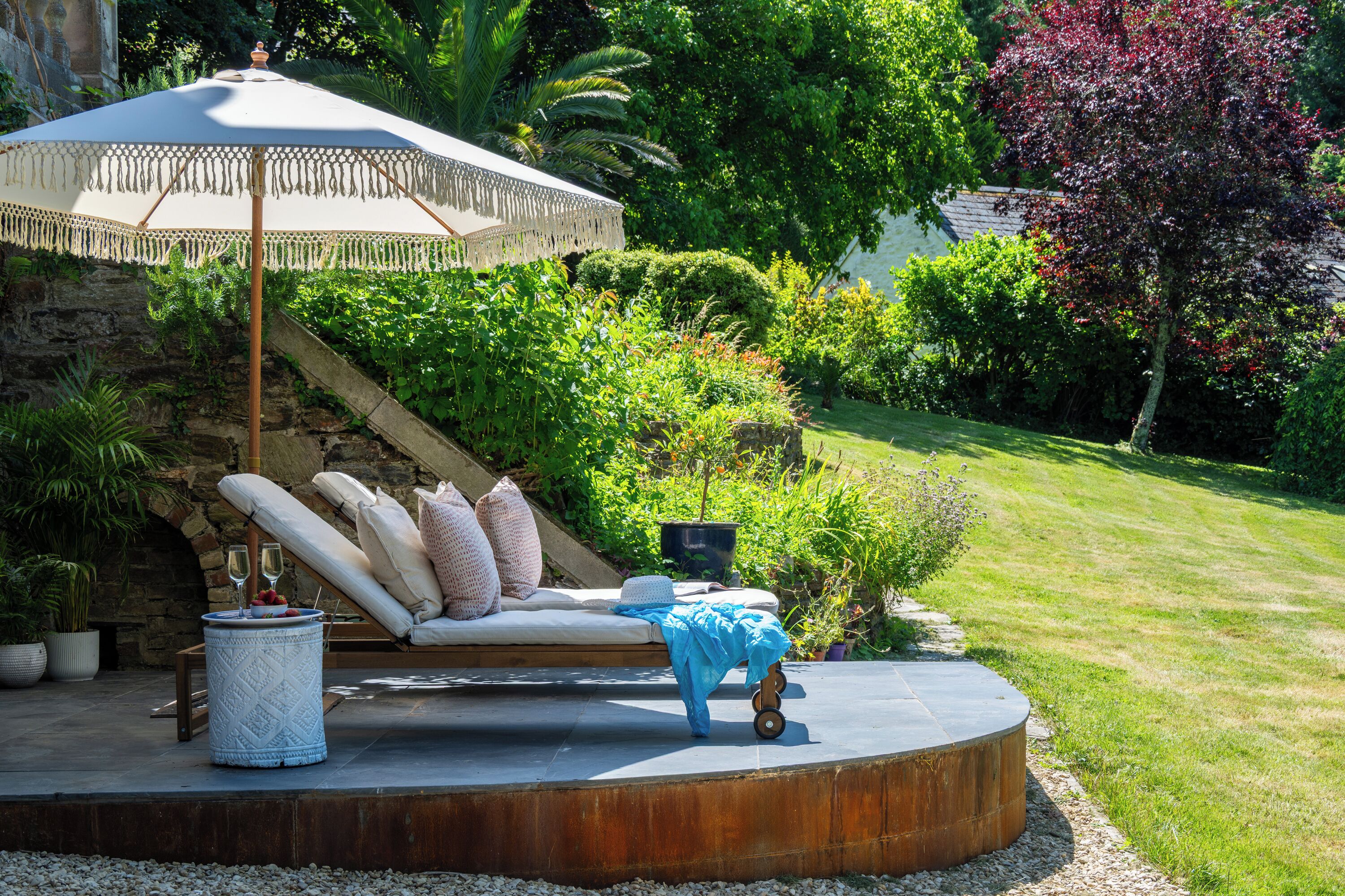 A circular outdoor seating area with a cushioned bench, a table with a blue cloth, and a decorative umbrella.