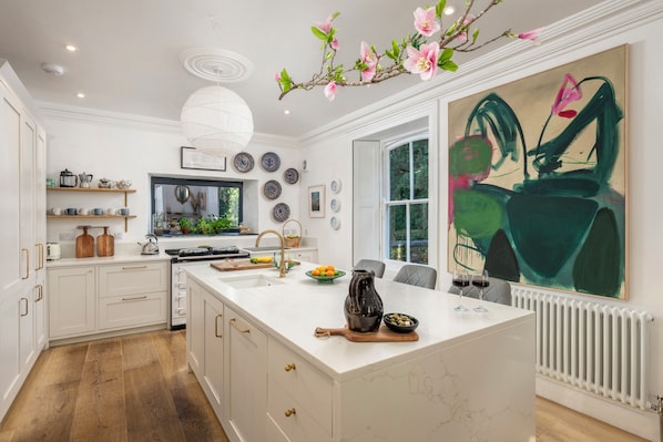 A modern kitchen with white cabinetry, a large island, and a dining area with a view of the garden.