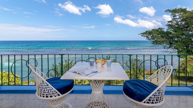 A balcony with a table and two chairs overlooking a beach. -  Waterfront ,  minutes from the beach, self catering, 24 hr security,            (Ocho Rios)