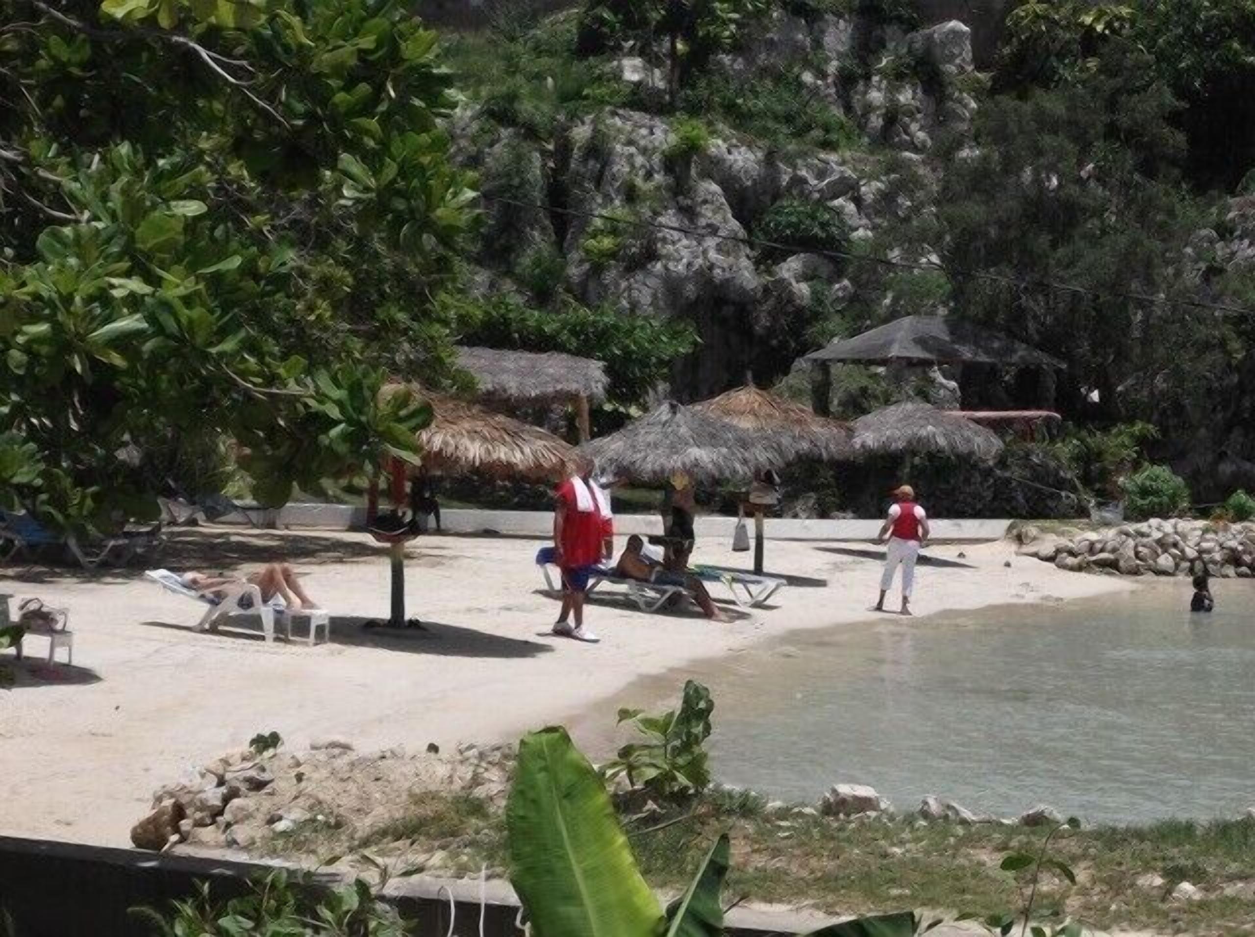 A beach with thatched umbrellas, lounge chairs, and rocky cliffs in the background.