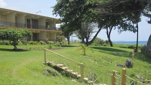A grassy area with a wooden staircase leading up to a building with a balcony. -  Waterfront ,  minutes from the beach, self catering, 24 hr security,            (Ocho Rios)