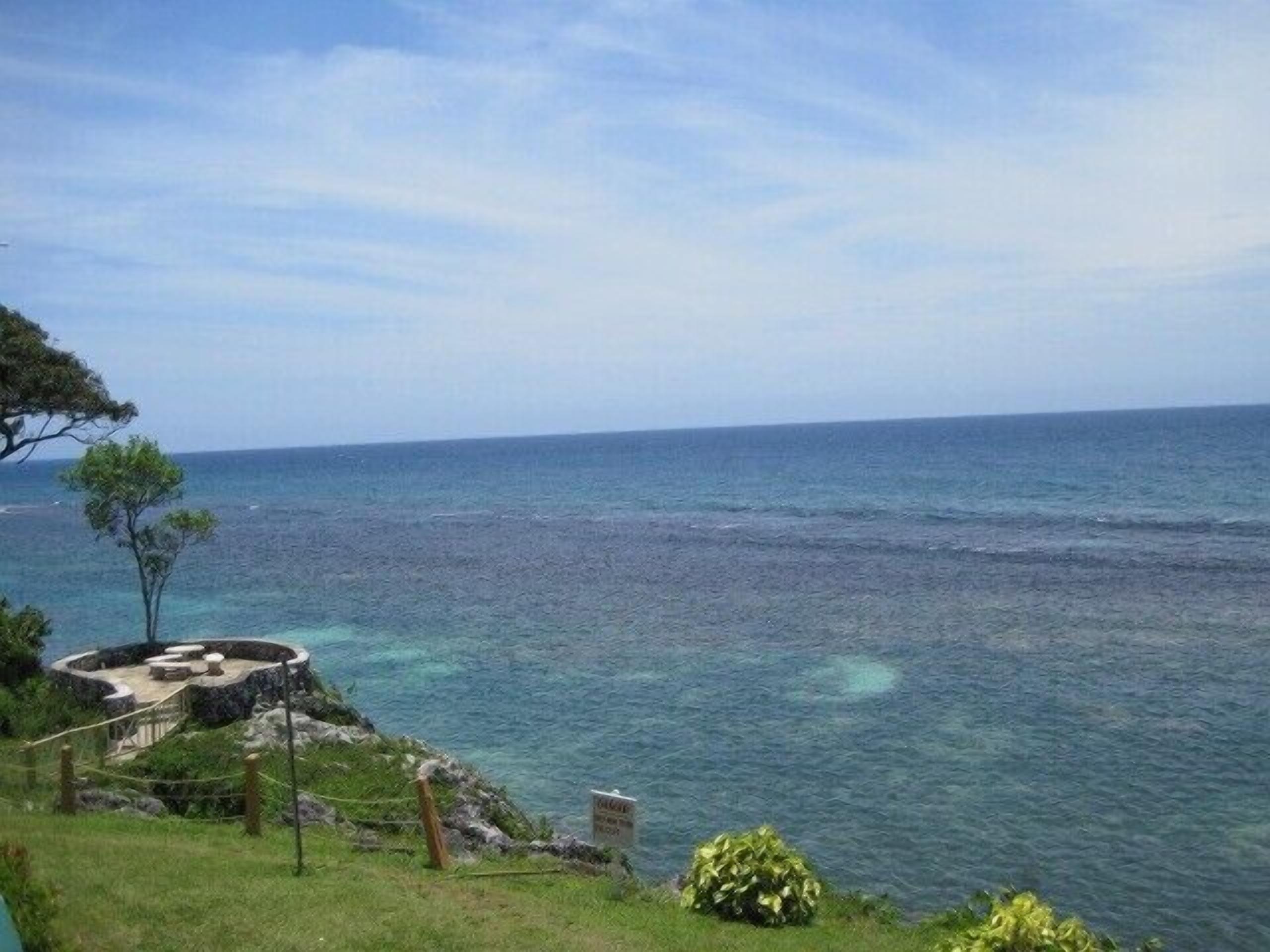 A coastal view with a clear sky, a rocky shoreline, and a circular stone structure with seating.