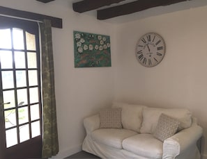 Ein gemütliches Zimmer mit einem weißen Sofa, einer Vintage-Uhr und einem Blumenbild an der Wand.