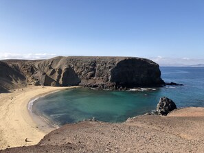 A coastal landscape with a sandy beach, rocky cliffs, and clear turquoise waters.