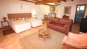A room with a bed, a sofa, a small table, and a wicker chair. There is a kitchen area in the background. - Quinta do Pântano is a calm and reserved place, with unique ambience and landscapes (Machico)