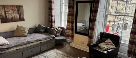 A cozy room with a sofa, a chair, a bed, a large mirror, and a view of the city through a window.