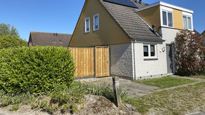 A two-story house with a sloped roof, a wooden gate, and a solar panel on the roof. - Holiday home at the beach in a holiday park (Wemeldinge)