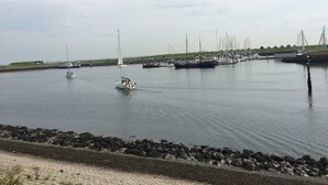 A marina with several boats docked, a sandy beach with rocks, and a grassy area in the background. - Holiday home at the beach in a holiday park (Wemeldinge)