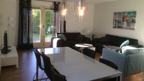 A modern living room with a dining area, featuring a large table, sofas, and a chandelier. - Holiday home at the beach in a holiday park (Wemeldinge)