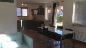 A modern living space with a dining area, kitchen, and a large window. - Holiday home at the beach in a holiday park (Wemeldinge)
