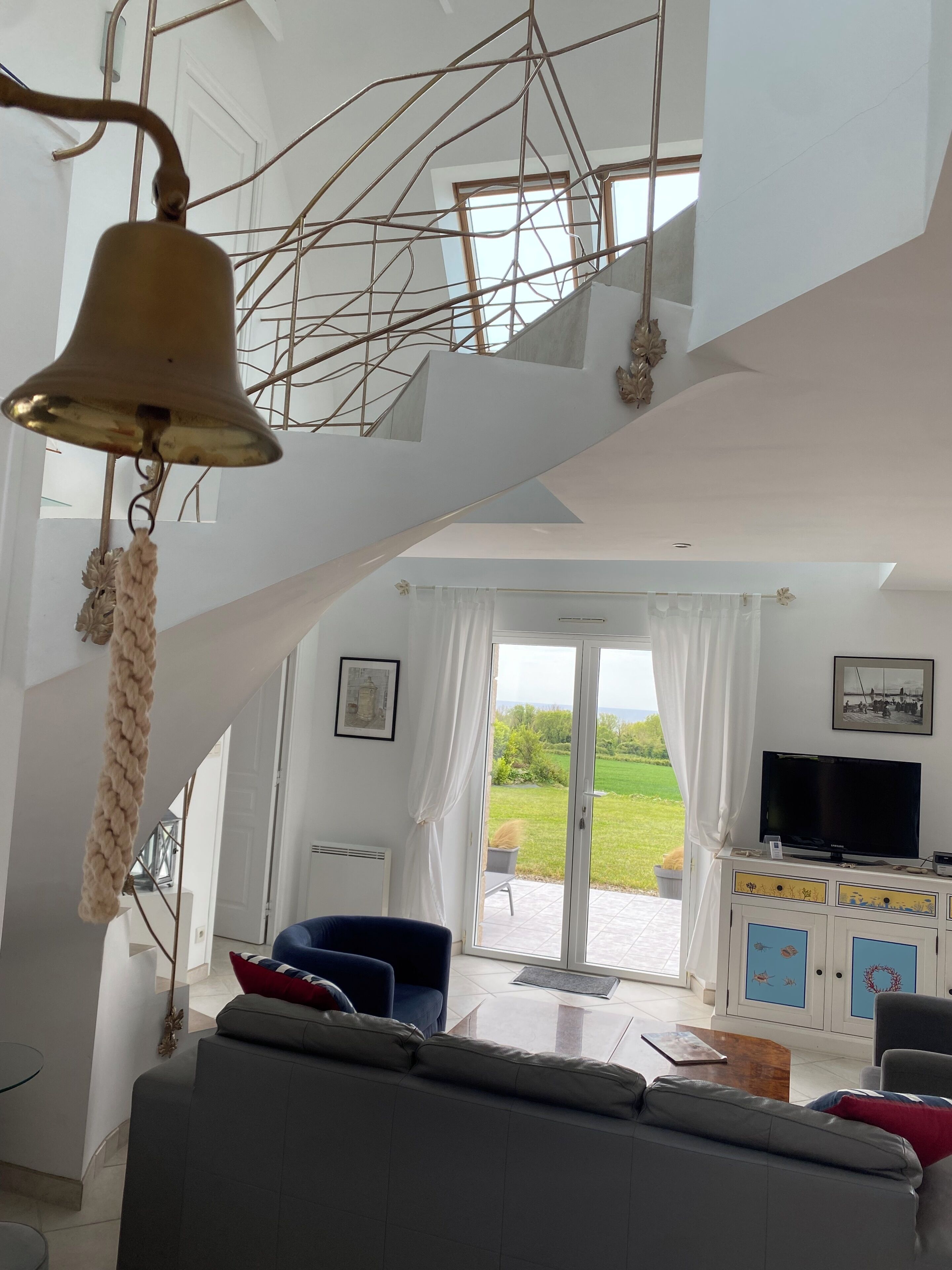 A modern interior with a staircase, a hanging bell, a sofa, a TV, and a view of the outdoors.