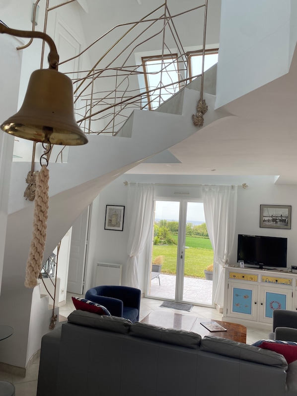 A modern interior with a staircase, a hanging bell, a sofa, a TV, and a view of the outdoors. - 180° SEA VIEW, BEACH NEARBY FOR THIS SPACIOUS ARCHITECT-DESIGNED HOUSE (Primelin)