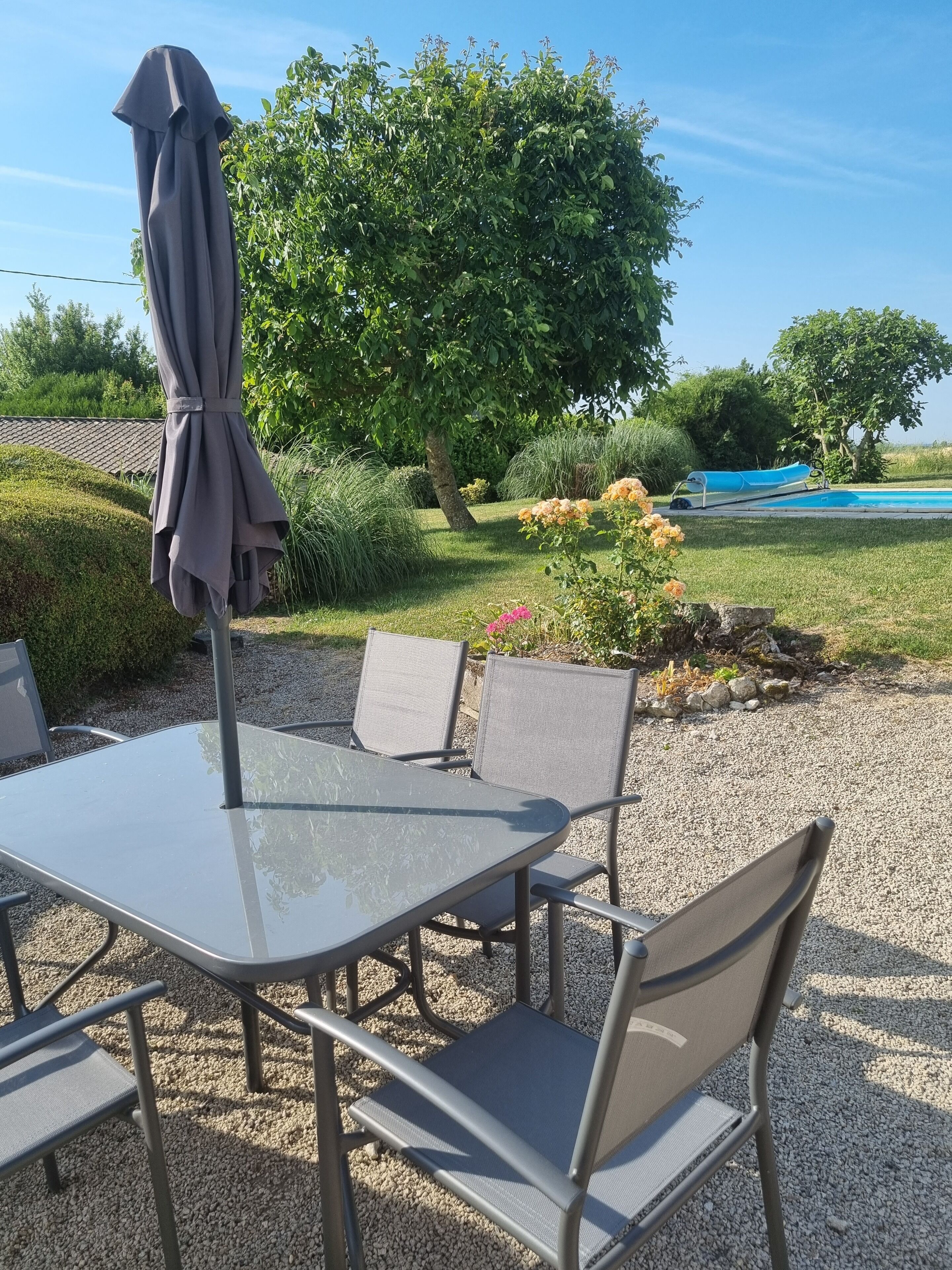 Un área de estar al aire libre con mesa y sillas, una sombrilla y vistas a una piscina y jardín.