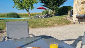 A table with croissants and orange juice, outdoor seating, a pool, and lounge chairs.