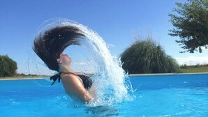 A person swimming in a clear blue pool with a tree and grassy area in the background.