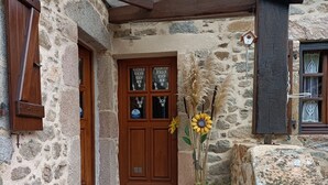 A stone building with a wooden door, a tiled entrance, and a small garden area with sunflowers. - country holiday home - LABASTIDE L'EVEQUE (Le Bas Ségala)