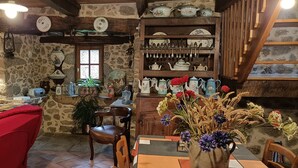 A rustic dining area with stone walls, wooden beams, and a variety of kitchenware displayed on shelves. - country holiday home - LABASTIDE L'EVEQUE (Le Bas Ségala)