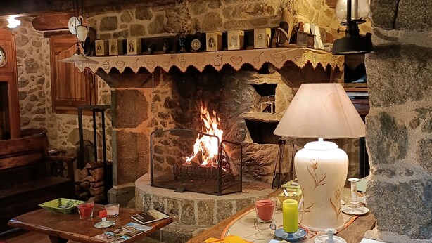 A cozy room with a stone fireplace, wooden furniture, and a table with drinks and a candle. - country holiday home - LABASTIDE L'EVEQUE (Le Bas Ségala)