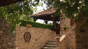 A stone building with a tiled roof, a stone wall with a wheel, and a gravel path. - country holiday home - LABASTIDE L'EVEQUE (Le Bas Ségala)