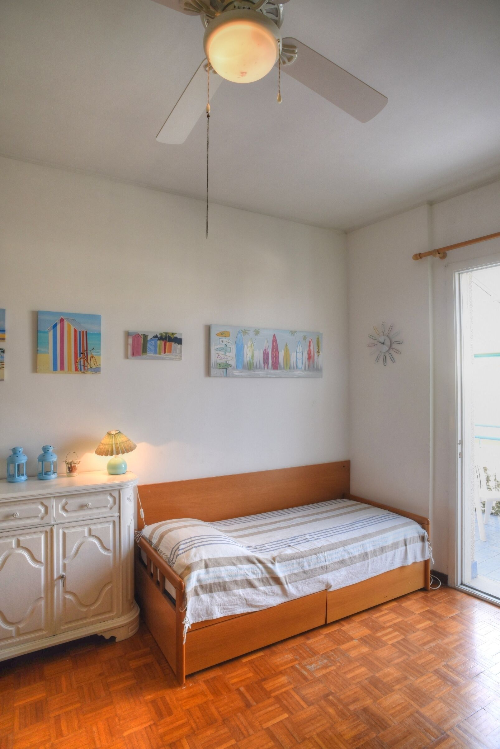 Een slaapkamer met een houten bed, een witte dressoir en een plafondventilator.