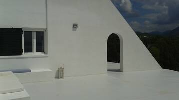A white building with a flat roof, a window with a shutter, and a small lantern on the roof.