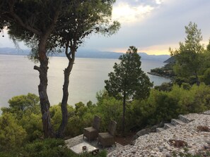 Une vue sur un lac, avec des arbres et un sentier en pierre menant à un espace de détente équipé de chaises en osier.