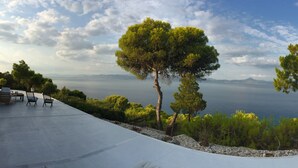 Eine Terrasse mit Blick auf das Meer, umgeben von Bäumen und einem weißen Gebäude.